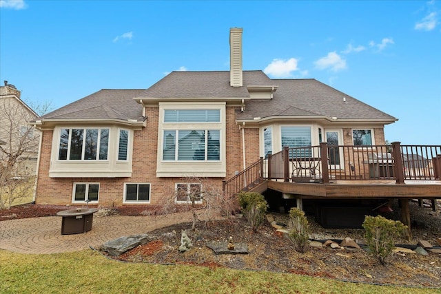 back of house featuring brick siding, roof with shingles, a chimney, a fire pit, and a wooden deck