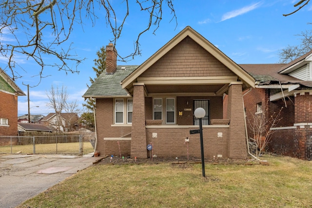 bungalow featuring brick siding, a chimney, a gate, fence, and a front yard