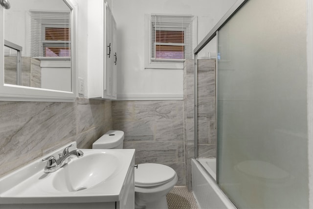 bathroom featuring enclosed tub / shower combo, vanity, toilet, and tile walls