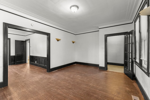 empty room featuring a wainscoted wall, wood finished floors, visible vents, baseboards, and crown molding