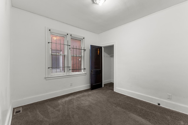 spare room featuring dark colored carpet, visible vents, and baseboards