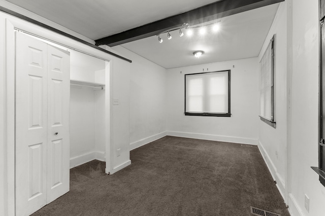 unfurnished bedroom with visible vents, dark carpet, beam ceiling, and baseboards