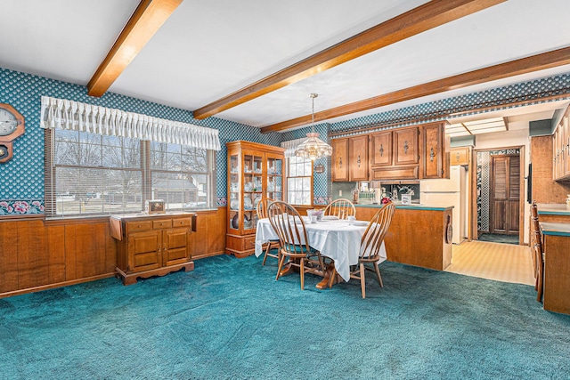 carpeted dining room with a chandelier, wainscoting, beamed ceiling, and wallpapered walls