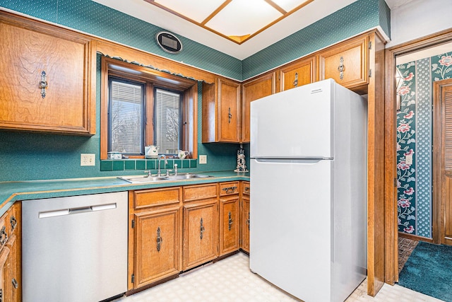 kitchen with brown cabinets, light floors, freestanding refrigerator, a sink, and dishwasher