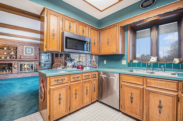 kitchen featuring a fireplace, light floors, stainless steel appliances, brown cabinetry, and a sink