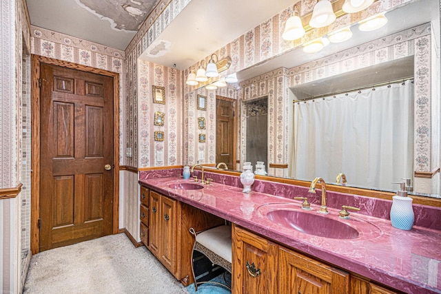 bathroom featuring double vanity, curtained shower, a sink, and wallpapered walls