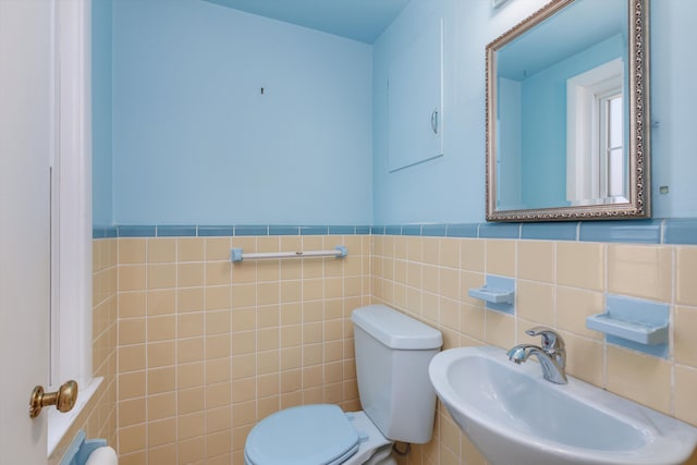 half bathroom with toilet, tile walls, a sink, and wainscoting