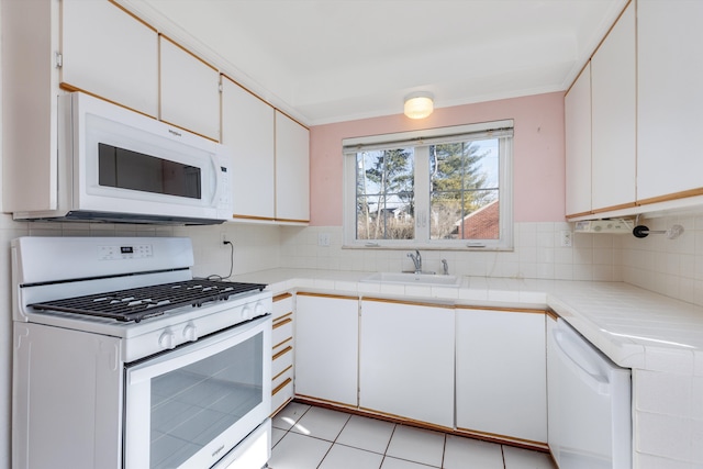 kitchen with white appliances, a sink, white cabinetry, tile counters, and decorative backsplash