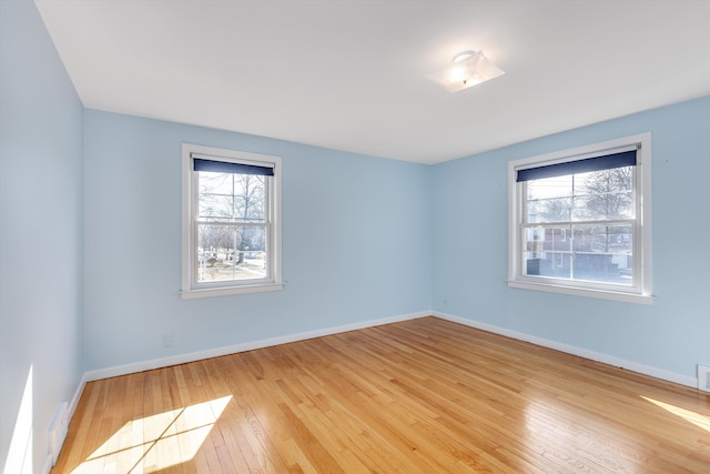 empty room with hardwood / wood-style flooring, visible vents, and baseboards