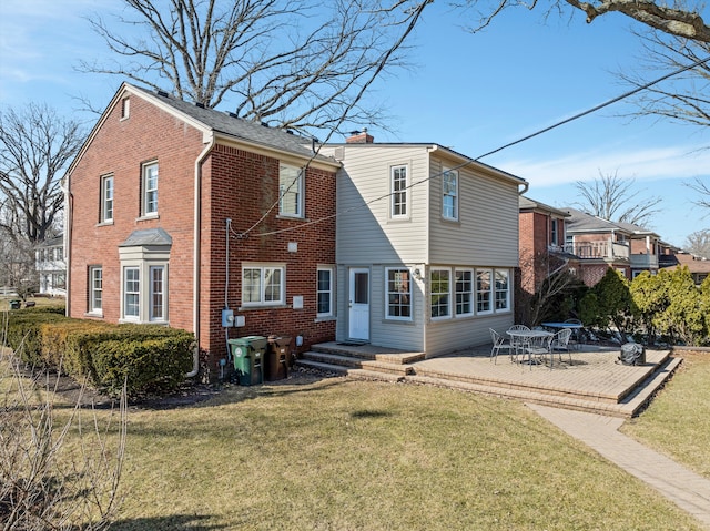 rear view of house with a yard, brick siding, a chimney, and a patio area