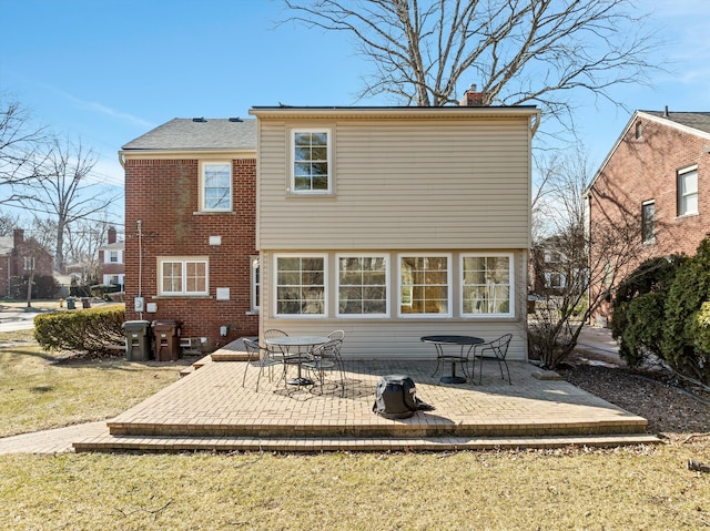 rear view of property with a patio, brick siding, a chimney, and a lawn