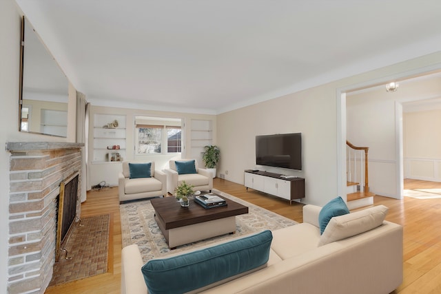 living area featuring a brick fireplace, stairs, built in shelves, and wood finished floors