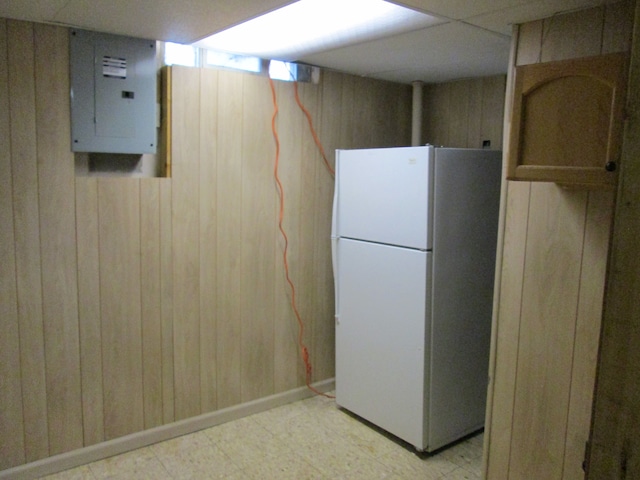 basement featuring wood walls, electric panel, light floors, and freestanding refrigerator