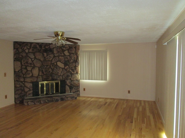 unfurnished living room with a textured ceiling, ceiling fan, a fireplace, and wood finished floors