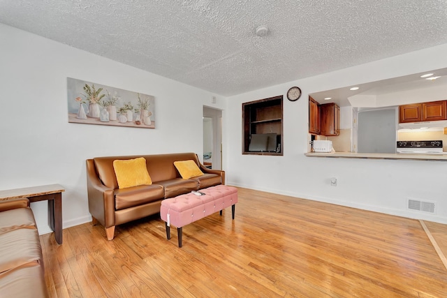 living area featuring baseboards, light wood-style flooring, visible vents, and a textured ceiling