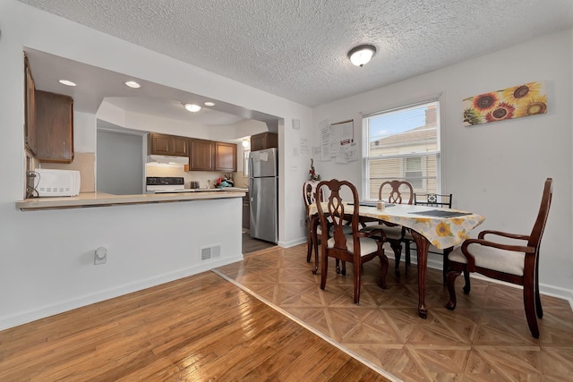 dining area with a textured ceiling, parquet flooring, visible vents, and baseboards