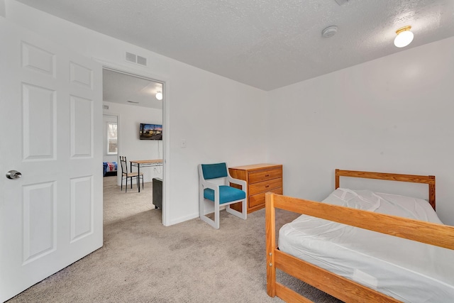 bedroom with light carpet, baseboards, visible vents, and a textured ceiling