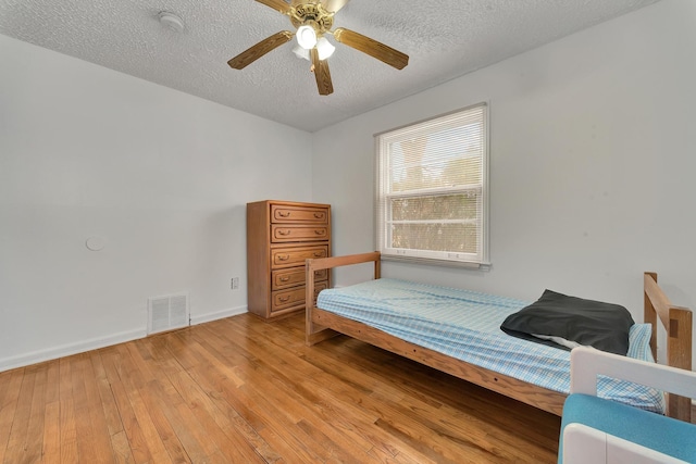 bedroom featuring visible vents, light wood-style flooring, ceiling fan, a textured ceiling, and baseboards