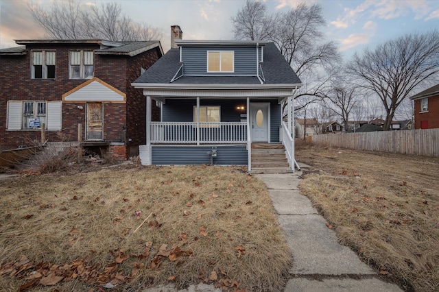 view of front of house with a shingled roof, a chimney, fence, a front lawn, and a porch