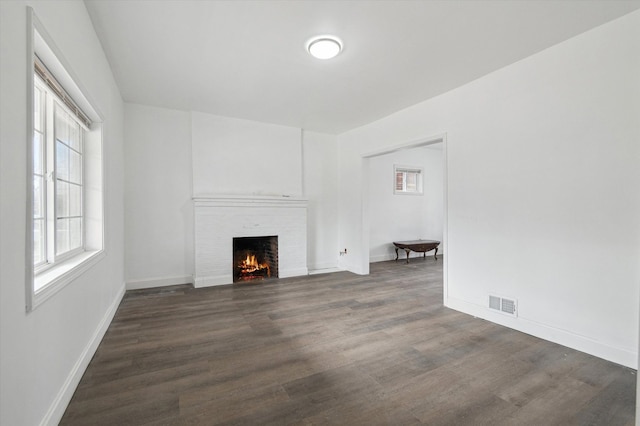 unfurnished living room featuring a brick fireplace, visible vents, baseboards, and wood finished floors