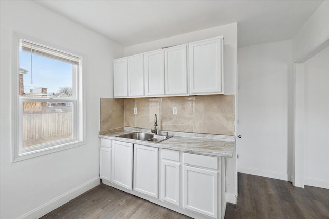 kitchen featuring light countertops, backsplash, dark wood-type flooring, a sink, and baseboards