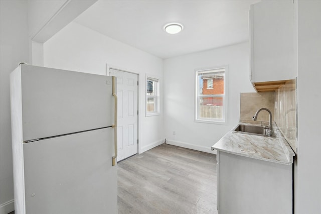 kitchen featuring light countertops, light wood-style flooring, freestanding refrigerator, a sink, and baseboards