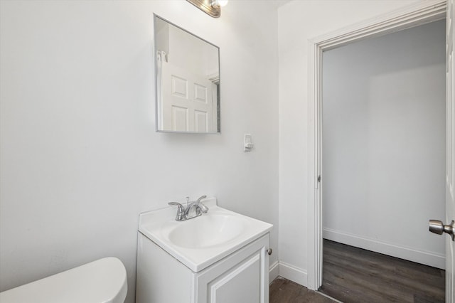 half bathroom with toilet, baseboards, wood finished floors, and vanity