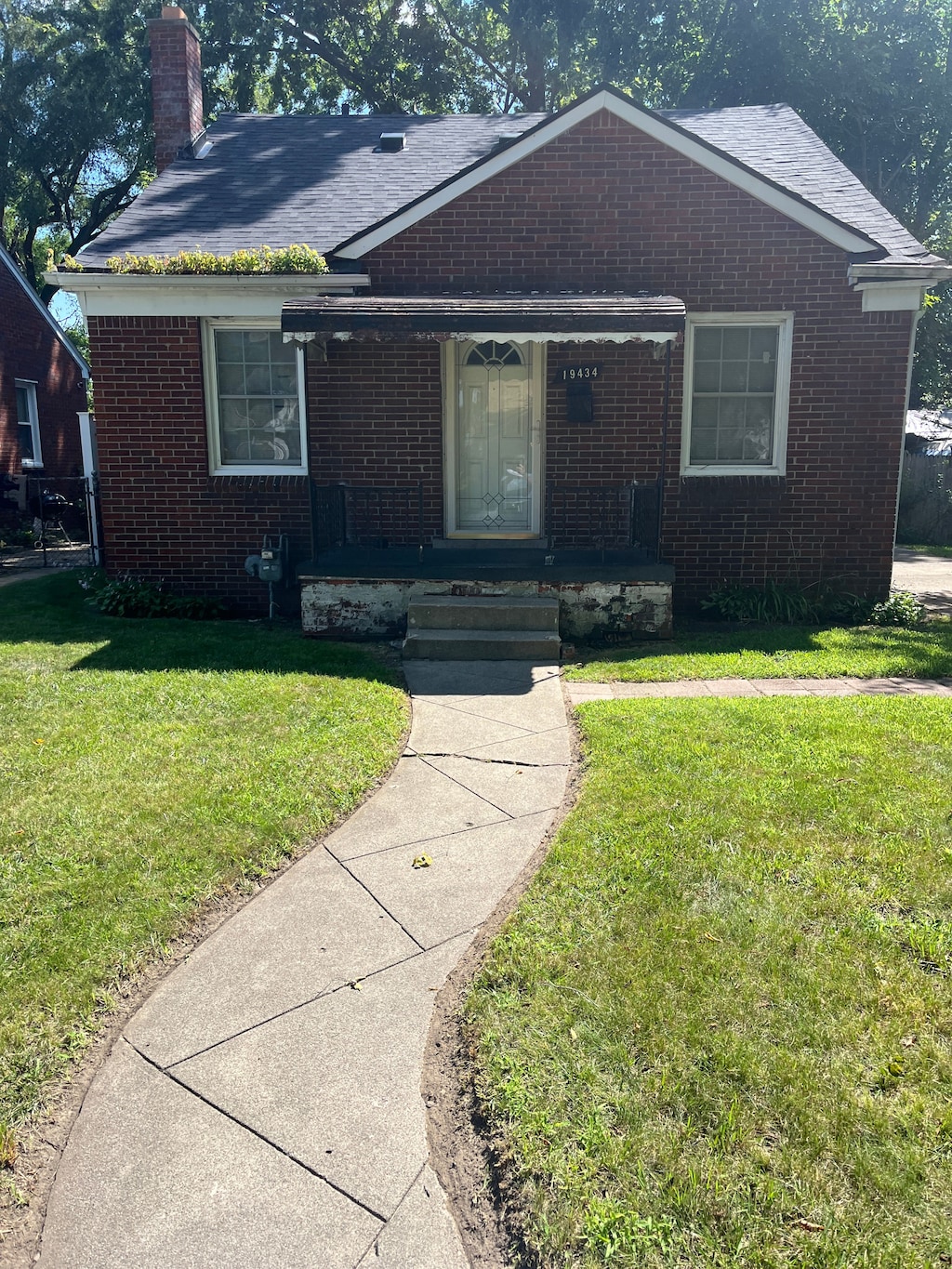 view of front of home featuring covered porch, brick siding, a chimney, and a front lawn