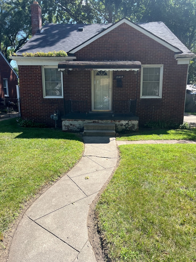 view of front of home featuring covered porch, brick siding, a chimney, and a front lawn