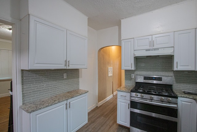 kitchen with arched walkways, wood finished floors, under cabinet range hood, stainless steel range with gas cooktop, and white cabinetry