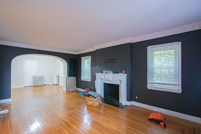 unfurnished living room featuring arched walkways, wood finished floors, a fireplace with flush hearth, and baseboards