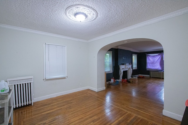 empty room with arched walkways, ornamental molding, wood finished floors, and baseboards