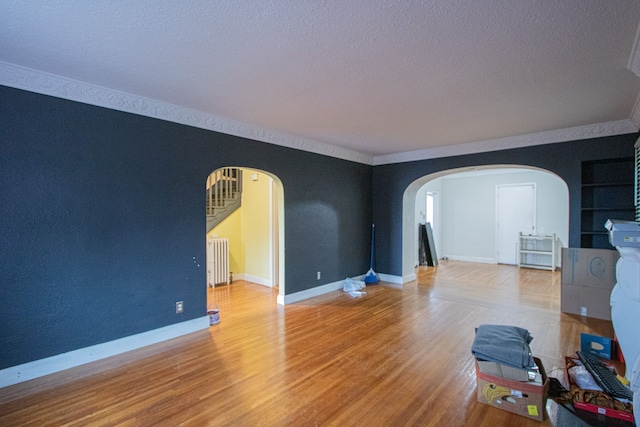 living area with arched walkways, radiator, a textured ceiling, wood finished floors, and baseboards