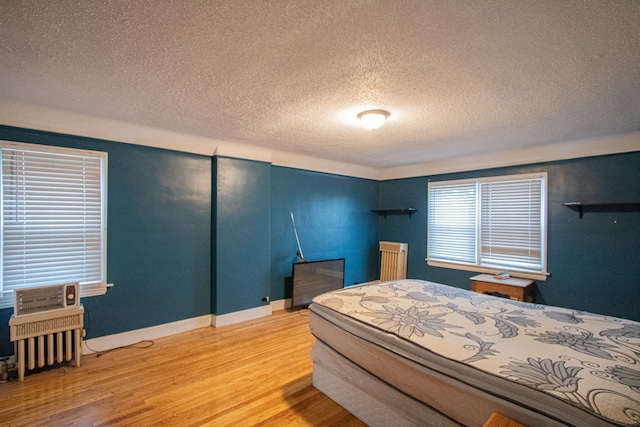 bedroom with radiator heating unit, a textured ceiling, baseboards, and wood finished floors