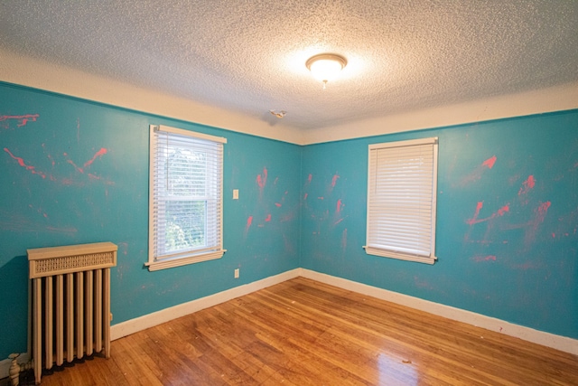 unfurnished room with radiator, a textured ceiling, baseboards, and wood finished floors