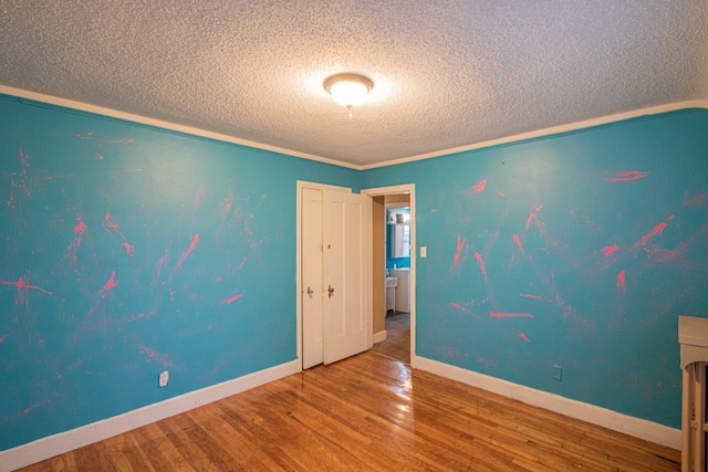 unfurnished bedroom with a textured ceiling, wood finished floors, and baseboards