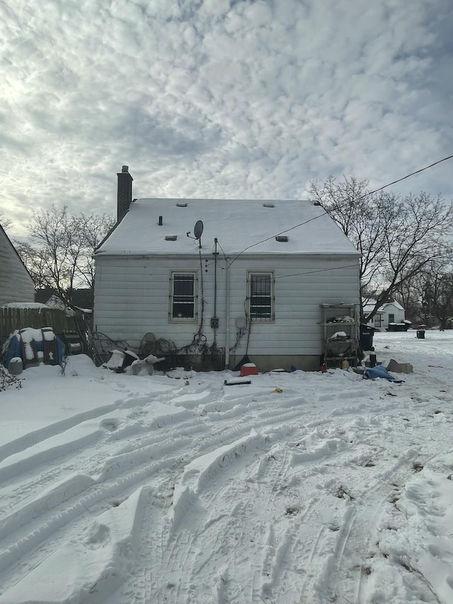 snow covered back of property with fence and a chimney