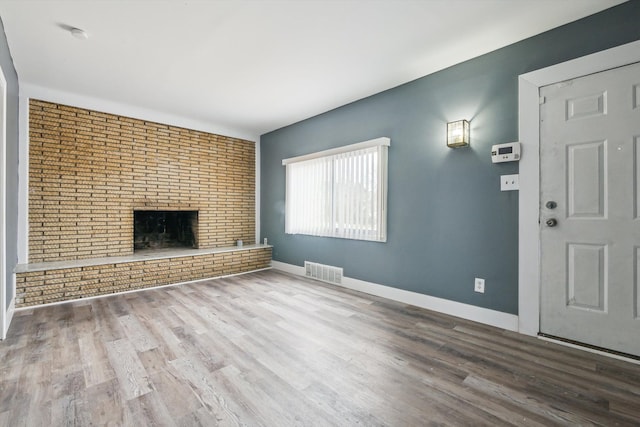 unfurnished living room with wood finished floors, visible vents, brick wall, baseboards, and a brick fireplace