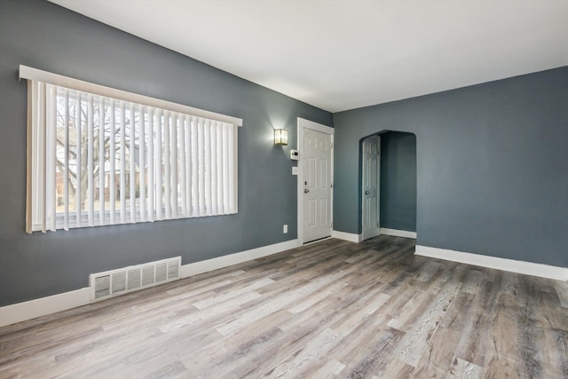 spare room featuring wood finished floors, arched walkways, visible vents, and baseboards