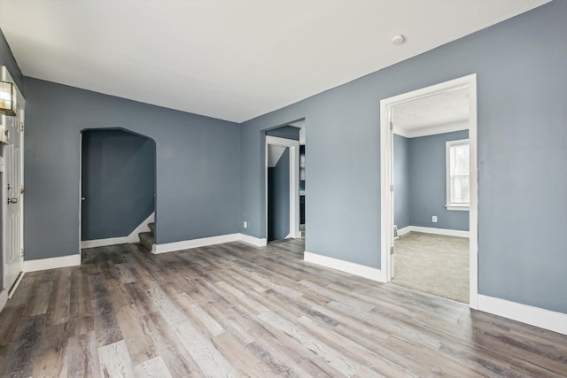 spare room featuring arched walkways, stairway, baseboards, and wood finished floors