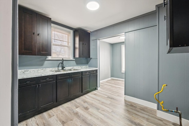 kitchen with a sink, light wood-type flooring, baseboards, and light stone countertops