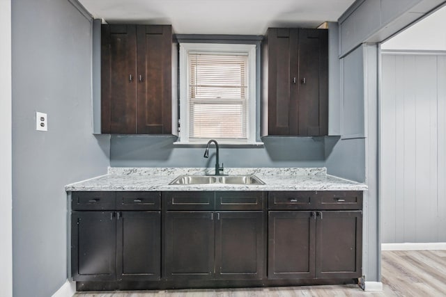 kitchen featuring dark brown cabinets, light stone countertops, light wood-style floors, and a sink