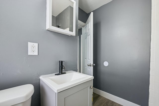 half bath with toilet, vanity, baseboards, and wood finished floors