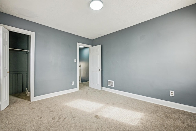 unfurnished bedroom with visible vents, a walk in closet, a closet, carpet flooring, and baseboards