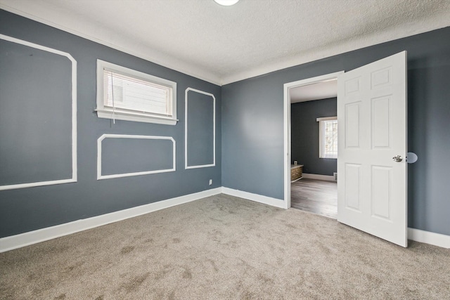 empty room with carpet flooring, a textured ceiling, and baseboards