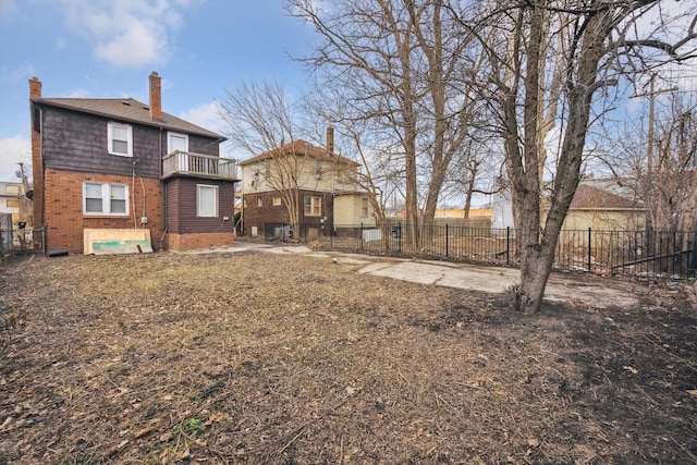 rear view of house featuring brick siding, fence, a chimney, a balcony, and crawl space