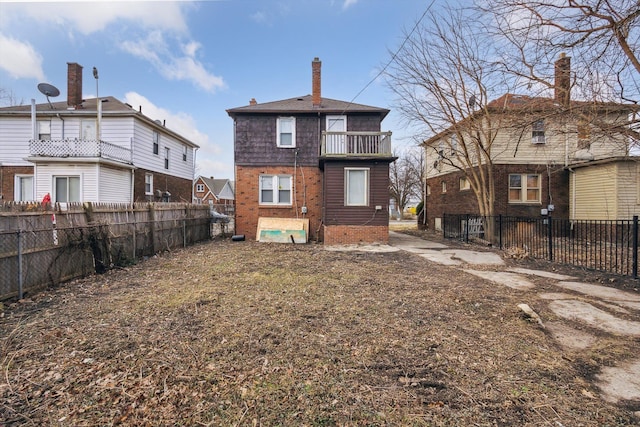 back of property with a balcony, fence private yard, brick siding, and a chimney