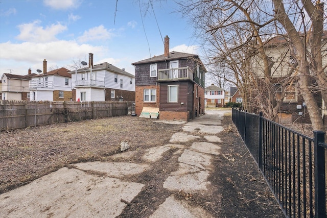 back of house featuring brick siding, a balcony, fence private yard, and a residential view