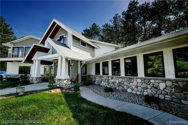 craftsman house featuring a balcony, stone siding, and a shingled roof