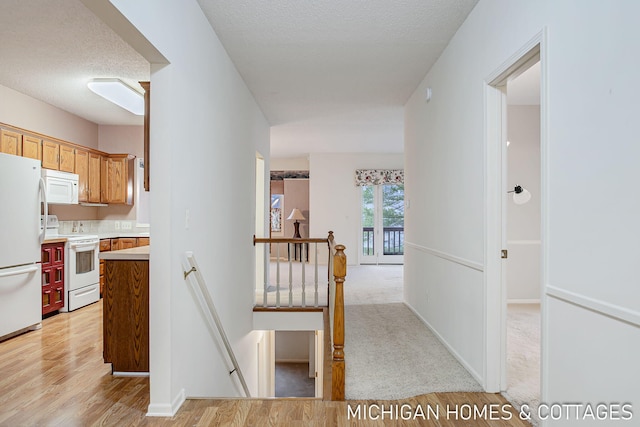 hallway with light wood finished floors, light carpet, a textured ceiling, an upstairs landing, and baseboards